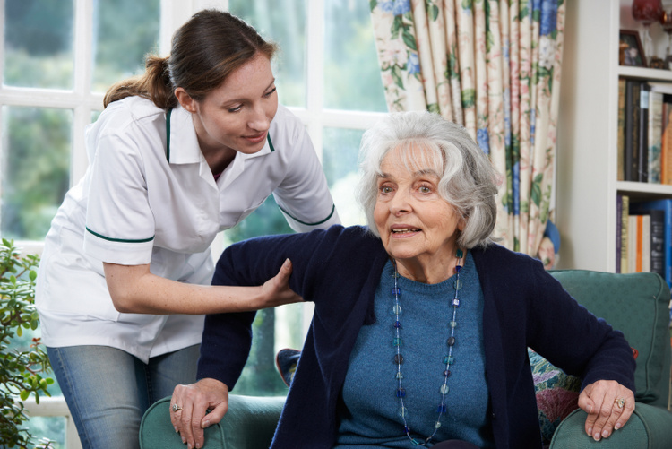 home care nurse in white helping elderly woman stand up in her own home